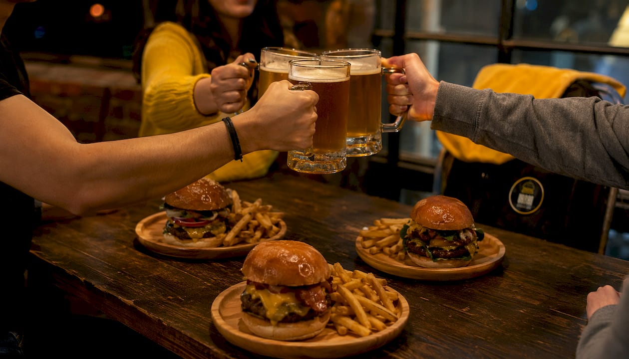 Una mesa llena de hamburguesas caseras, rodeada de gente disfrutando de la comida entre risas y buen ambiente.