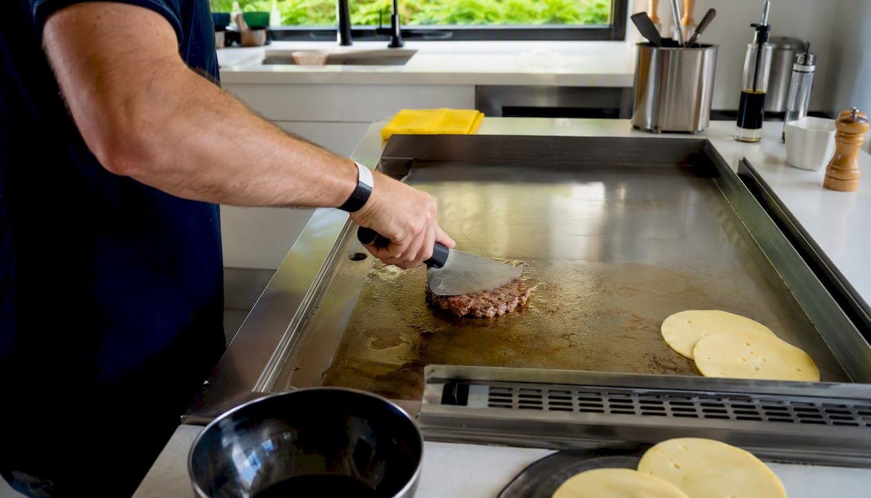 El cocinero aplasta la carne de la hamburguesa sobre la sartén bien caliente.