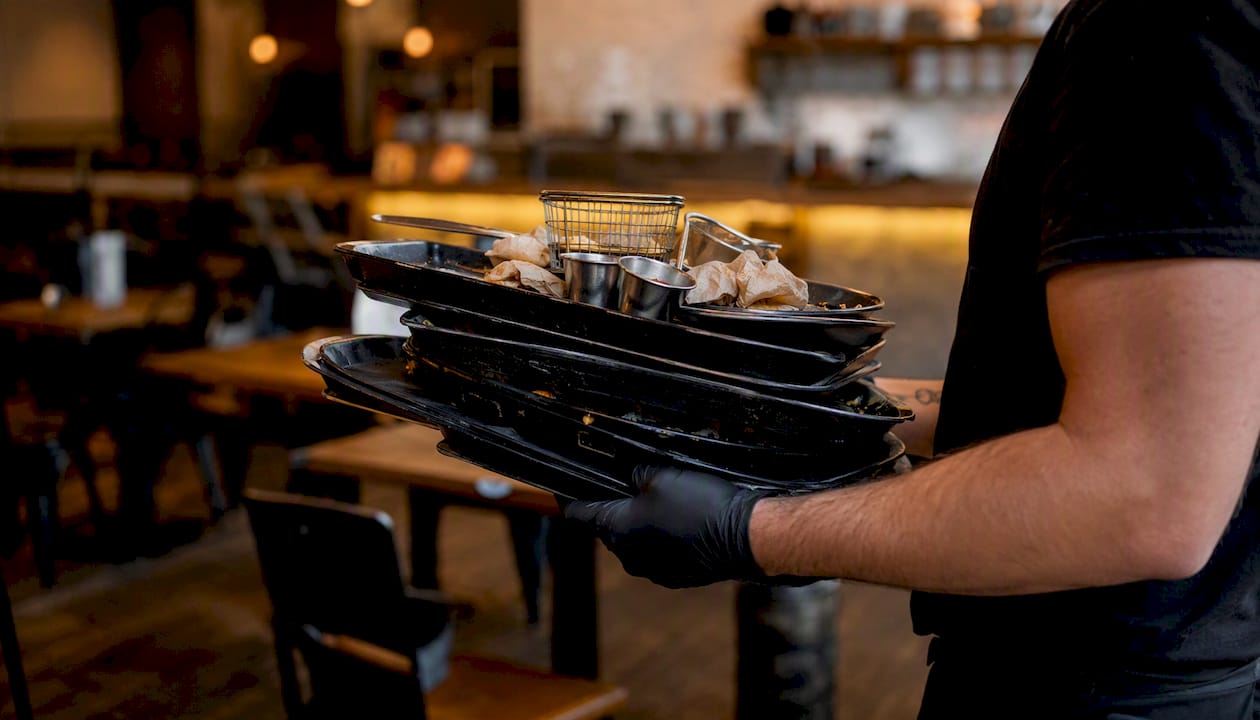 Un camarero recoge los platos de una mesa grande después de que el grupo ha terminado de comer.