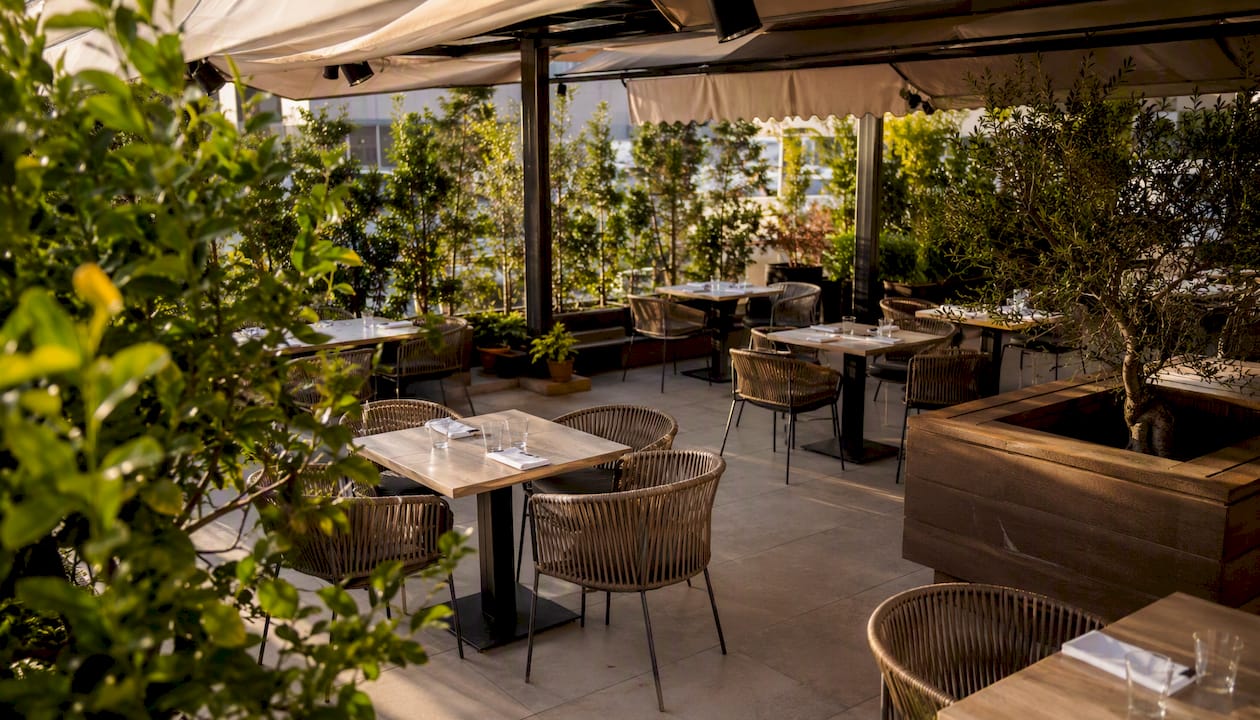 Mesas vacías en la terraza de un restaurante, iluminadas por el sol.