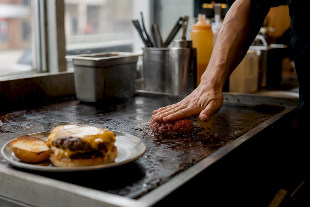 Chef aplastando la hamburguesa de carne en la plancha