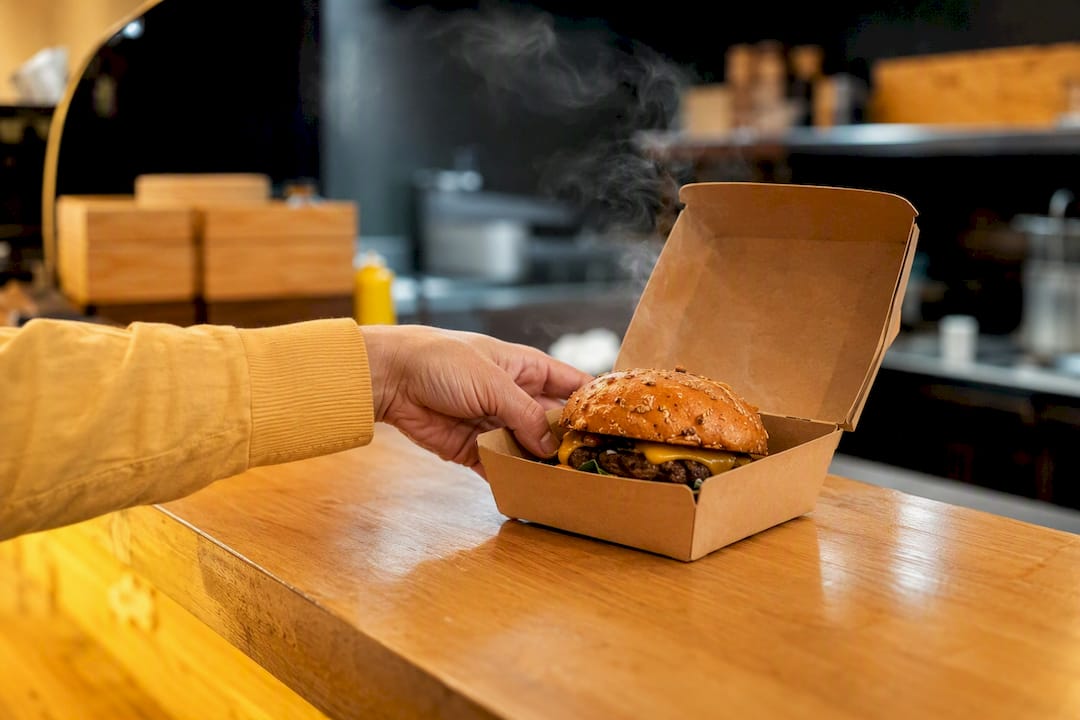 Mano levantando caja de hamburguesa para llevar desde el mostrador
