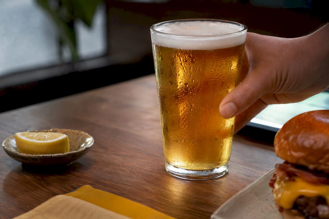 Cerveza al lado de una hamburguesa parcialmente visible