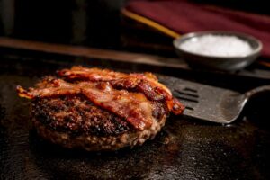 Hamburguesa con tocino dorándose en la plancha