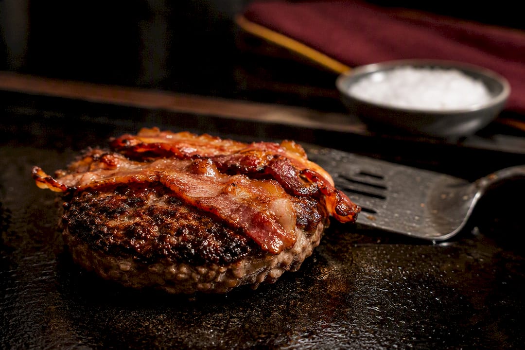 Hamburguesa con tocino dorándose en la plancha