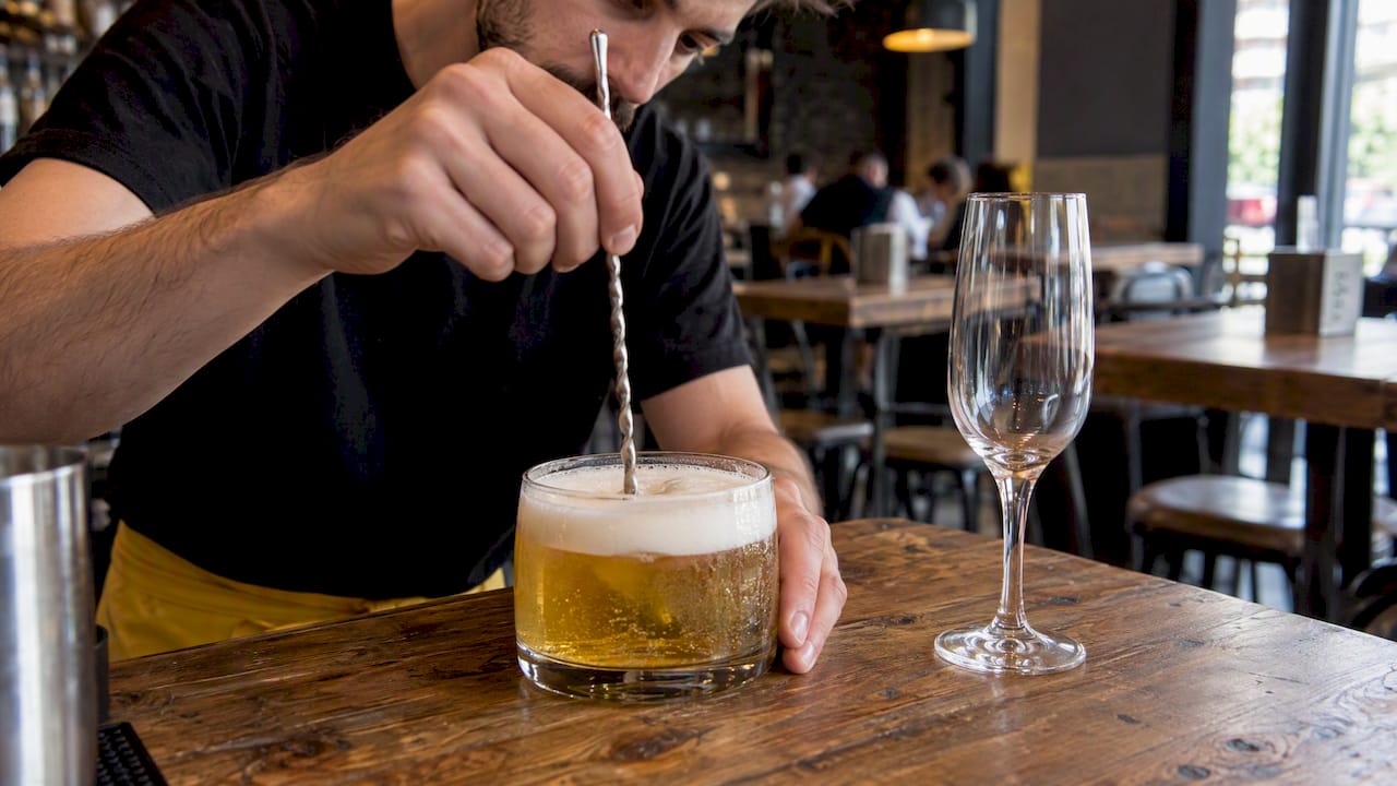 Camarero mezclando un cóctel en un vaso ancho